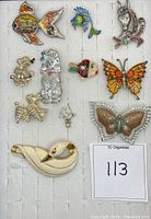 Top view of 11 animal-shaped brooches arranged on a white organizer. Includes enamel and metal fish, cats, dogs, butterflies, and a duck.