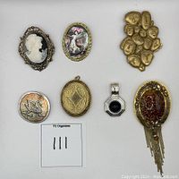 Top view of seven assorted vintage jewelry pieces: cameos, brooches, pendants. Variety of metal tones and stones.