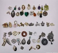 Top-down photo showing an assortment of costume jewelry charms and small pendants of various shapes and colors spread out in rows on a white background.