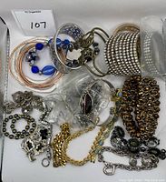 Photo showing a variety of bracelets including bangles, cuffs, chained and elastic styles, some with decorative stones and beads, in a container with label '107'