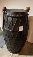 Full view of the Indian drum showing the black laced cord design and round-headed drumsticks resting on top.