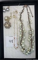 Top view of a collection of Dior faux pearl grey stud earrings paired with multiple mixed faux pearl necklaces, drop earrings, floral brooch, and ring pieces laid in a jewelry display tray.