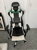 Front view of S-Racer black and white gaming chair with armrests, caster wheels, and a decorative green garland around headrest.
