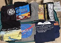 Photo showing seven men's T-shirts with different logo prints arranged on a green surface.
