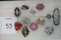 Top view of 11 rhinestone rings arranged on white background, showing diverse designs and colors.