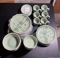 Top view showing 6 dinner plates, 5 lunch plates, 6 cups, 6 saucers, 5 bowls, and 6 fruit bowls arranged on a dark surface highlighting the bamboo pattern and green crackle glaze.
