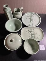 Front view of the seven-piece Saan Celadon serving ware set showing vase, water pitcher, round platter, rectangular platter, lidded bowl, and two bowls.