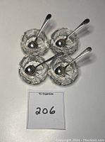 Four clear crystal salt cellars with silver-plated spoons placed inside them, showing overall set configuration.