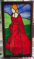 Front view of the stained glass window showing woman in red dress, with green hills and blue sky background.