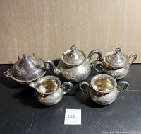 Full set arranged on black surface showing all five items including teapot, creamer, sugar bowl, butter dish, and waste cup with lids visible
