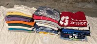 Photo showing three stacks of t-shirts arranged on a sheet, one stack of plain colors and two stacks of various logo/event tees