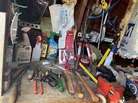 Photo of assorted hand tools, spray bottles, garden treatment containers, and metal vices on a shelf in a backyard closet.