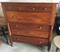 Front view of the antique wooden dresser showing six drawers and turned legs. One missing drawer pull point visible. Surface scratches and keyhole details visible.