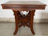 Front view of antique wooden table showing rectangular top and ornate carved base with curved legs and central finial.