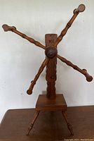 Full view of antique wooden wool winder standing on a brown surface against white background, showing five curved arms and rectangular base with legs.