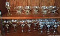 Photo showing the main set of stemmed glasses including 10 medium (6 in) and 8 large (6.5 in) glasses plus 10 dessert bowls on a wooden shelf.