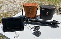 Lot contents on white table outdoors: two binocular cases, Quantaray tripod, Kodak digital photo frame with remote and power adapter