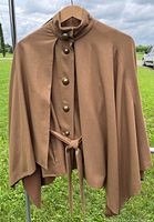Brown cape jacket with a belted vest design and metallic buttons hanging outdoors