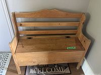 Frontal view of wooden storage bench showing carved top backrest and hinged seat lid with green sticker indicating dimensions.
