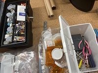 White plastic organizer box holding tools including pink-handled pliers and a small screwdriver, with some embellishments visible nearby.