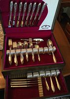Full view of the flatware laid in the wooden box with velvet lining, showing knives, forks, spoons organized in compartments.