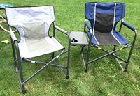 Two folding outdoor chairs on grass, one with collapsible table and cup holder attached.