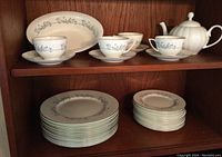 Top shelf showing white tea cups, saucers with floral pattern and a white tea pot. Large oval serving bowl behind.