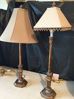 Pair of table lamps with matching distressed copper metal bases and different style beige fabric shades shown side by side against a dark background.