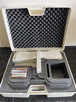 Open carrying case showing foam-padded interior with the white embroidery unit and slots for accessories.