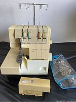 Front angled view of the cream-colored Pfaff Hobbylock 786 electronic sewing machine showing threading dials, needle, and detached taped plastic front cover with pouch of spools beside.