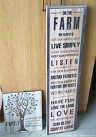 Photo of two wooden plaques leaning against wooden cabinetry; larger plaque with black text 'On The Farm' inspirational message; smaller plaque with tree graphic and family message