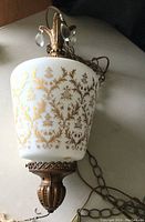Close-up front angle of the milk white glass swag lamp showing gold decorative patterns and attached hanging chain.