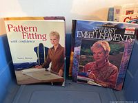 Photo of two sewing books: 'Pattern Fitting with Confidence' and 'New Easy Sew Embellishments',' showing the cover with author Nancy Zieman.
