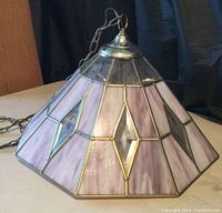 Side angled view of the pyramid-shaped stained glass chandelier showing purple, white, and clear glass panels with silver tone outlines and hanging chain.