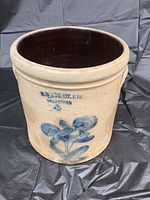 Full front view of a beige stoneware crock with stamped text and blue floral design