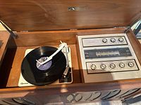 View of the open stereo console showing the built-in Garrard turntable with a record on it and radio tuner with control knobs.