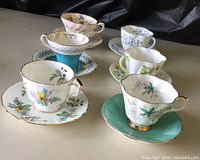Photo showing six teacup and saucer sets arranged in two rows featuring various floral patterns and gold trim.