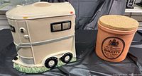 Photo showing side and top view of beige ceramic horse trailer cookie jar next to terracotta-colored biscuit jar with cork lid, both placed on black cloth surface.