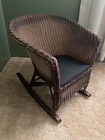 Front and side view of the wicker rocking chair, showing woven seat, back, armrests, and cushion.