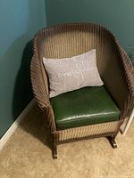 Front angled view of wicker rocker chair with green vinyl cushion and 'grateful' pillow (not included).