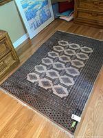 Full view of rug on hardwood floor showing overall shape, pattern and fringe ends