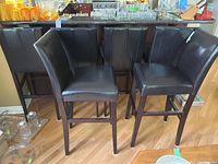 Set of six black faux leather bar stools with dark wooden legs arranged near a countertop.