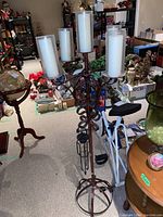 Full view of iron floor-standing candelabra with five frosted glass candle holders, placed in basement room with furniture and other items around.
