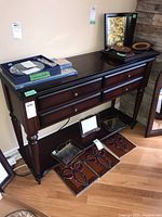 Full view of the console table showing all four drawers, top surface with some items, and lower shelf with items underneath.