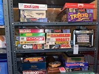 Shelf with three rows of assorted board games including Monopoly, Urban Myth, Tribond, Clue, Risk, and others.