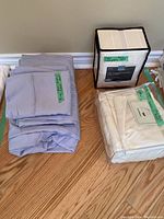 Stack of light grey king size bed linens including flat sheet, fitted sheet, and pillowcases with green tape labels.