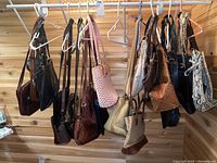 Wide view of handbags and purses hanging on rack in wooden room, showing variety of colors and textures including leather and fabric.