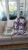 Two quilts displayed on a couch. One is a floral scalloped edge quilt, the other is a multicolor Wedding Ring Quilt with interlocking rings design.