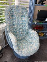 Front view of the blue painted rattan swivel chair with floral seat and back cushion, showing the high back and contoured armrests.