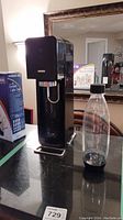 Black SodaStream soda maker dispenser with textured front panel and metal base stand shown on tabletop.